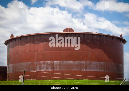 Enorme serbatoio di olio arrugginito nella fattoria di carri armati in Cushing Oklahoma dietro recinzione con filo spinato con abbastanza sfondo blu cielo Foto Stock