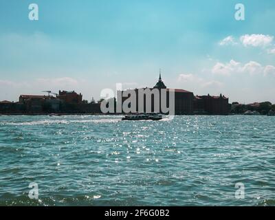 Sul terminal dei traghetti a Venezia, Italia. Vista a contrasto sull'isola di Giudecca. Acque blu in una giornata estiva soleggiata e limpida. Viaggi in Europa Foto Stock