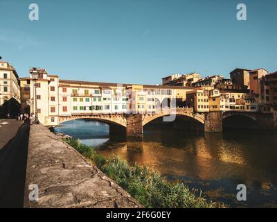 Ponte Vecchio ponte ad arco segmentato con spandrel chiuso che attraversa il fiume Arno al tramonto a Firenze, Italia. Vista dall'argine con specchio luminoso Ref Foto Stock