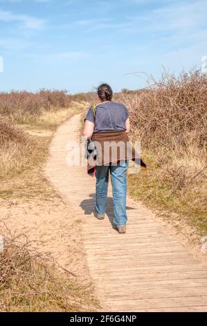 Una donna che cammina sul lungomare attraverso le dune della riserva naturale di Home Dunes sulla costa nord del Norfolk. Foto Stock