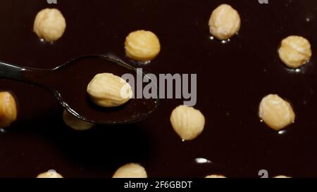 Cioccolato fondente liquido scuro e nocciole girevoli, processo di preparazione dolci con frutta a guscio Foto Stock