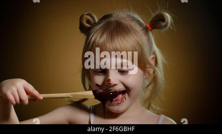 Gioiosa bambina sorridente con faccia sporca da fusa cioccolato su sfondo scuro in studio Foto Stock
