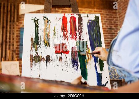 Pittore dello studio che crea un quadro astratto su tela utilizzando dipinti ad olio e coltello a palette. Giovane artista femminile che lavora. Processo creativo, relax Foto Stock