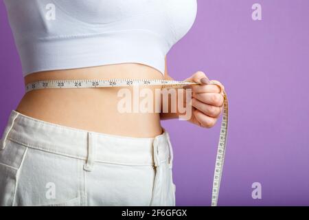 La donna sottile misura la vita con un nastro di misurazione. Concetto sano di perdita di peso di forma del corpo. Ventre sottile in vita piccola in grandi pantaloni isola bianchi Foto Stock