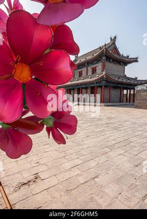 Xian, Cina - 30 aprile 2010: Mura della città di Huancheng. Anno del display Tiger. Primo piano di falso fiore rosa con edificio storico grigio e pillola di marroon Foto Stock