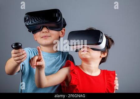 Un ragazzo caucasico e una ragazza con cuffie per realtà virtuale stanno giocando a multiplayer. Un concetto futuristico con i bambini che sono in una dimensione diversa Foto Stock