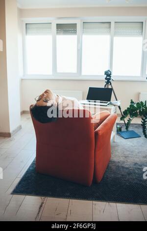 La giovane donna caucasica sta sdraiata su un divano gesturando la stanchezza mentre hai una lezione video online Foto Stock