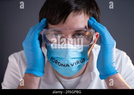 Stanco, esausto, devastato medico scienziato, dopo un lungo turno, testa in mani sulla maschera facciale con il testo coronavirus. Concetto di speranza persa, malattia di Covid-19 Foto Stock