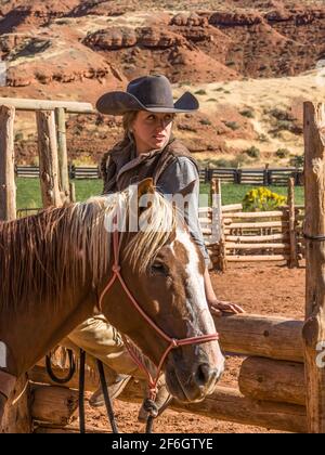 Un giovane di lavoro attraente cowgirl wrangler siede su una rampa di legno recinzione dal suo cavallo in un ranch vicino a Moab, Utah. Foto Stock