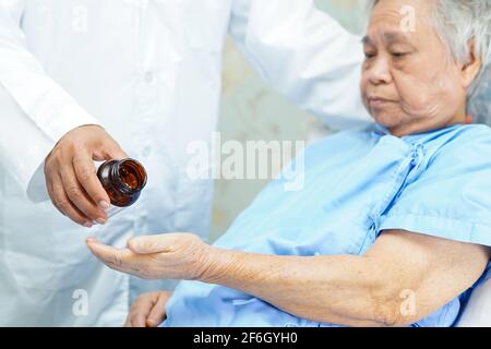 Medico asiatico che tiene e versa le pillole di antibiotici medicina dal flacone al paziente per il trattamento dell'infezione in ospedale: Concetto di farmacia. Foto Stock