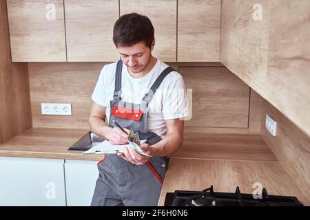 L'idraulico in uniforme firma un contratto per servizi nel cucina Foto Stock