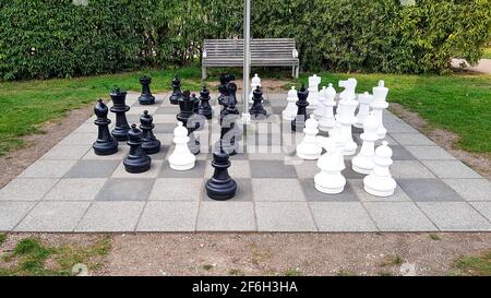 Gioco di scacchi nel parco esterno nel gigante verde campo area pavimento scacchi figure bianco nero ricreazione hobby torneo tempo libero strategia estate Foto Stock