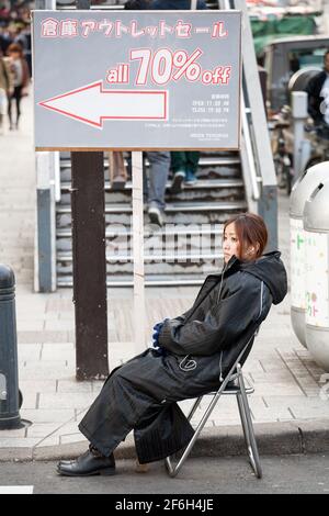 Donna giapponese seduta sulla strada accanto alla vendita di pubblicità cartelloni, Omotesando, Tokyo, Giappone Foto Stock