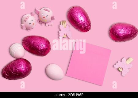 Sfondo pasquale rosa con uova di Pasqua, decorazioni e carta da note rosa bianca appiccicosa. Foto Stock