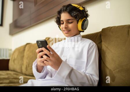 Ragazzo arabo a casa con cuffie e cellulare Foto Stock