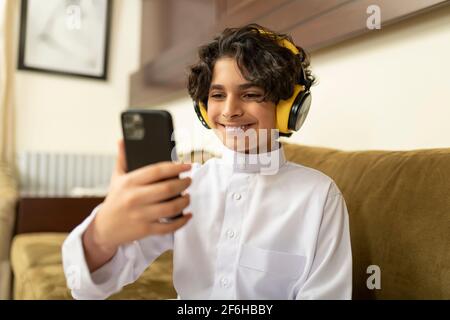 Ragazzo arabo a casa con cuffie e cellulare Foto Stock