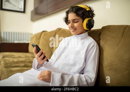 Ragazzo arabo a casa con cuffie e cellulare Foto Stock