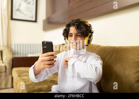 Ragazzo arabo a casa con cuffie e cellulare Foto Stock