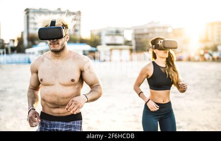 Giovane coppia che corre in spiaggia con un visore per la realtà virtuale - concetto di sport e tecnologia con amici jogging ed esercizio Foto Stock