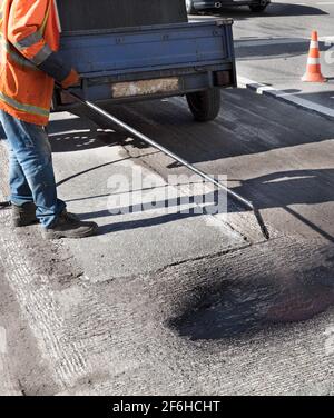 Un lavoratore spruzzi bitume su un vecchio asfalto pavimentazione durante la riparazione parziale e il ripristino di una strada asfaltata. Foto Stock