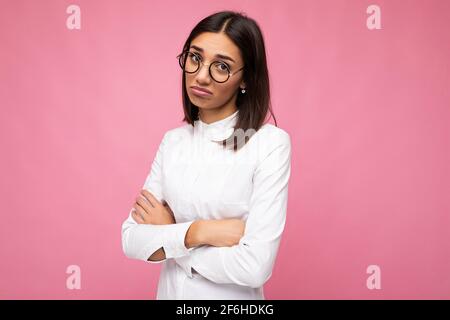 Giovane e attraente donna con bruna toccante che indossa abiti eleganti tutti i giorni e moderni occhiali ottici isolati sulla colorata parete di sfondo Foto Stock