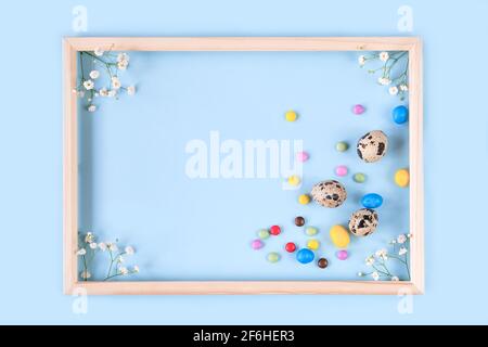 Carta di Pasqua con fiore di iride, uova di quaglia, caramelle colorate su sfondo blu. Foto Stock