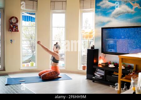 Bella donna che allunga le braccia mentre fa yoga in lei appartamento accogliente Foto Stock
