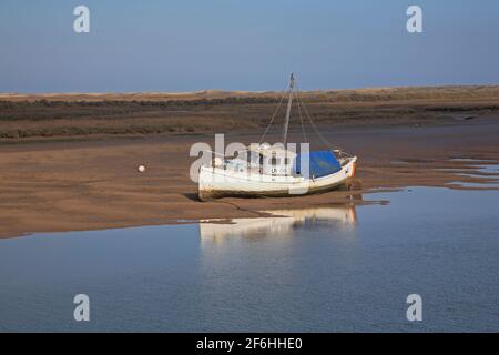 Una vista di una barca da pesca costiera con riflessi spiaggiati su appartamenti in acque basse a Overy Creek a Burnham Overy Staithe, Norfolk Inghilterra, Regno Unito. Foto Stock