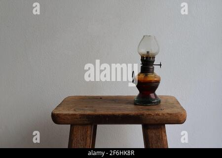 Closeup vintage kerosene lampada in piedi su sedia di legno vintage contro muro di cemento bianco Foto Stock