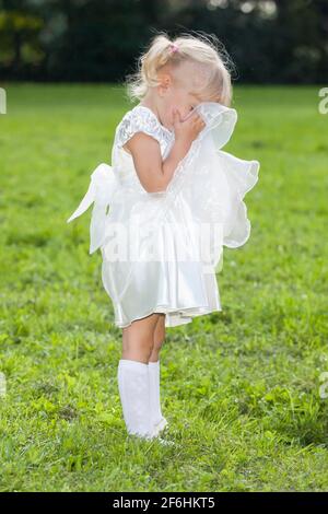 Bambina in abito bianco piange coprendo il viso. Foto di alta qualità Foto Stock