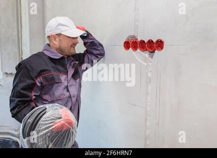 Un elettricista si trova contro la parete con un cavo elettrico per le prese. Primo piano Foto Stock