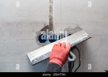 L'elettricista intonacerà fori e canali per prese e fili. Riparazione di appartamenti. Primo piano Foto Stock