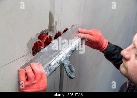 L'elettricista intonacerà fori e canali per prese e fili. Riparazione di appartamenti. Primo piano Foto Stock