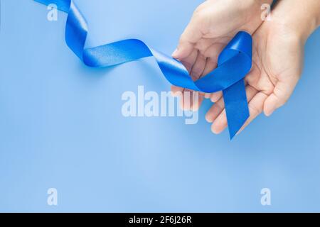 Mani che tengono il nastro blu profondo su sfondo blu con spazio per la copia. Cancro colorettale consapevolezza cancro del colon di persona anziana e mondo diabete giorno Chi Foto Stock