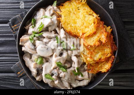 Vitello svizzero di Zurigo con funghi in salsa cremosa con frittelle di patate da vicino in un piatto sul tavolo. Vista dall'alto orizzontale Foto Stock