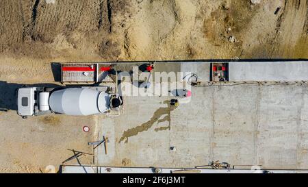 Sopra la vista dall'alto, i lavoratori edili stanno utilizzando il rastrello per lo spandimento e il listello metallico per il livellamento di calcestruzzo fresco in trincea quadrata dopo la colata Foto Stock