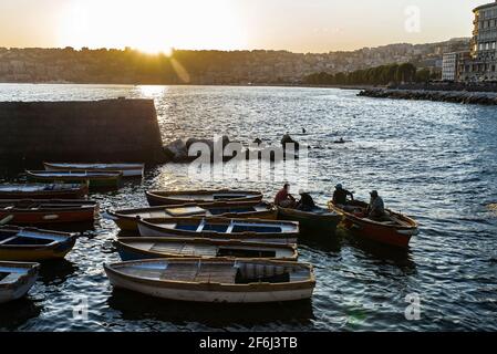 Napoli, Italia - 9 settembre 2019: Pescatori nelle loro vecchie barche da pesca in legno ormeggiate su un molo vicino al Castel dell'Ovo al tramonto Foto Stock