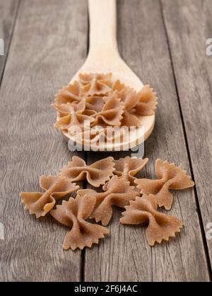 Pasta di farfalle integrale su un cucchiaio su un tavolo di legno. Foto Stock