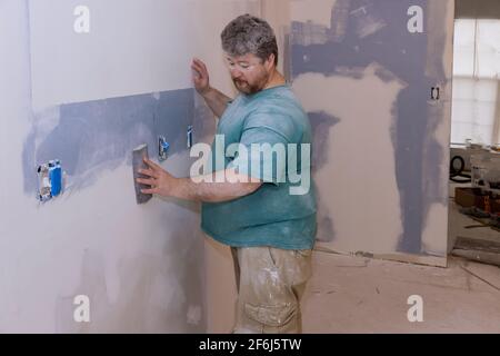 Il contraente che utilizza un cazzuola di sabbia levigando il muro a secco sulla parete Foto Stock