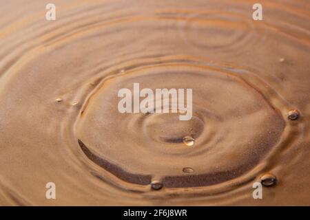 Sulla superficie dell'acqua, ci sono cerchi di gocce e bolle. Sotto l'acqua, si può vedere il fondo sabbioso. Immagine di sfondo Foto Stock
