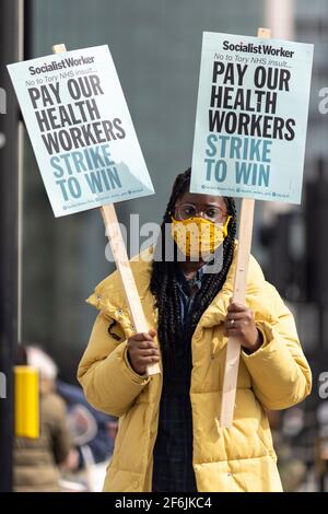 Londra, Regno Unito. 1 aprile 2021. Un manifestante che tiene i cartelli che leggono 'paga i nostri operatori sanitari, Sciopero per vincere'. I lavoratori dell’NHS hanno protestato per la proposta di un aumento salariale dell’1% da parte del governo al di fuori del St Thomas’ Hospital, Westminster Bridge Road, Londra, Regno Unito. Credit: Joshua Windsor/Alamy Live News Foto Stock