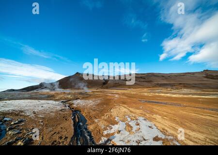 Namafjall Hverir zona geotermica in Islanda. Splendido paesaggio di valle dello zolfo con fumarole fumanti e cielo blu nuvoloso, sfondo di viaggio Foto Stock