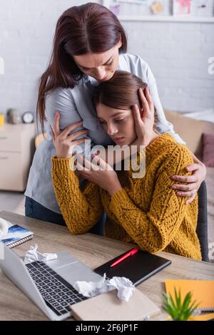 madre preoccupata che abbracciava la figlia adolescente triste studiare da casa Foto Stock