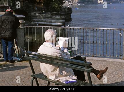 L'anziano si siede sulla panchina con la rivista Lake Como, Como, Italy Foto Stock