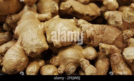 Le radici di zenzero (Zingiber officinale) in un mercato vegetale tradizionale sparso in modo poco chiaro con fuoco selettivo, primo piano full frame. Foto Stock
