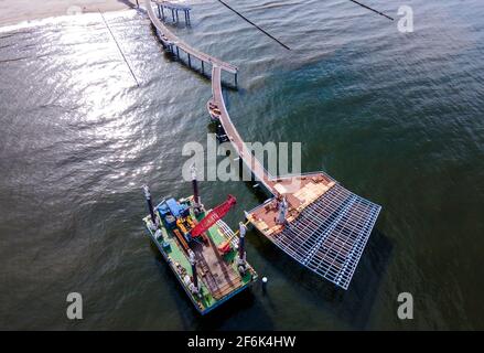 22 marzo 2021, Meclemburgo-Pomerania occidentale, Koserow: Un pontile galleggiante con una gru si trova accanto al nuovo molo in costruzione sull'isola di Usedom. A causa della necessaria sostituzione di alcuni legni tropicali posati come tavole da corsa e la rinnovata galvanizzazione dei segmenti di ringhiera, il ponte sarà ora pronto per il festival del ponte solo all'inizio di luglio 2021. Il molo si estende per quasi 300 metri nel Mar Baltico, e la forma curva del molo diritto su altri ponti è impressionante. La nuova costruzione costerà più di cinque milioni di euro. (Foto scattata con un drone) Foto: Jens Büt Foto Stock