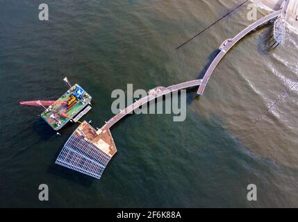 22 marzo 2021, Meclemburgo-Pomerania occidentale, Koserow: Un pontile galleggiante con una gru si trova accanto al nuovo molo in costruzione sull'isola di Usedom. A causa della necessaria sostituzione di alcuni legni tropicali posati come tavole da corsa e la rinnovata galvanizzazione dei segmenti di ringhiera, il ponte sarà ora pronto per il festival del ponte solo all'inizio di luglio 2021. Il molo si estende per quasi 300 metri nel Mar Baltico, e la forma curva del molo diritto su altri ponti è impressionante. La nuova costruzione costerà più di cinque milioni di euro. (Foto scattata con un drone) Foto: Jens Büt Foto Stock