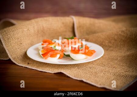 metà delle uova bollite con pezzi di salmone salato un tavolo di legno Foto Stock