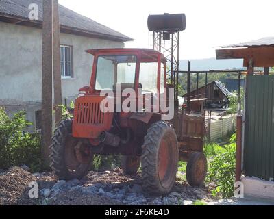 Un vecchio trattore rosso si trova su un percorso interrotto in campagna residenziale Foto Stock