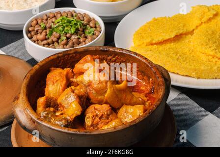 Pollo di Capoeira con couscous brasiliano, abbinato a riso, fagioli, manioca e vinaigrette, su un piatto bianco in cima a una linguetta a scacchi bianca e nera Foto Stock